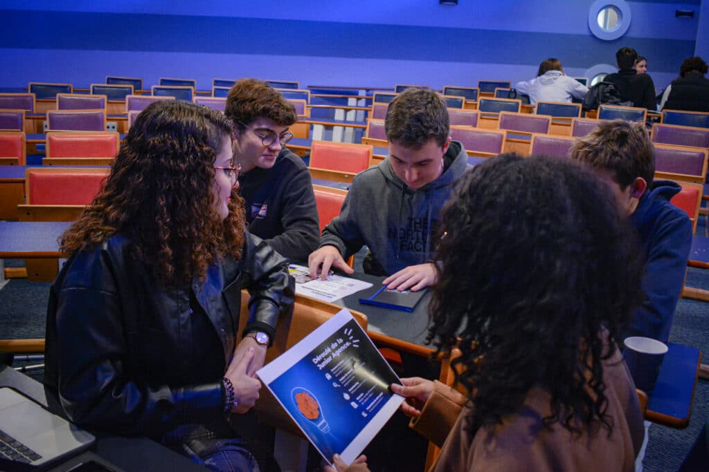 Des jeunes en groupe dans un amphithéâtre regardent des documents expliquant le déroulé d'une journée d'immersion à l'ISEFAC